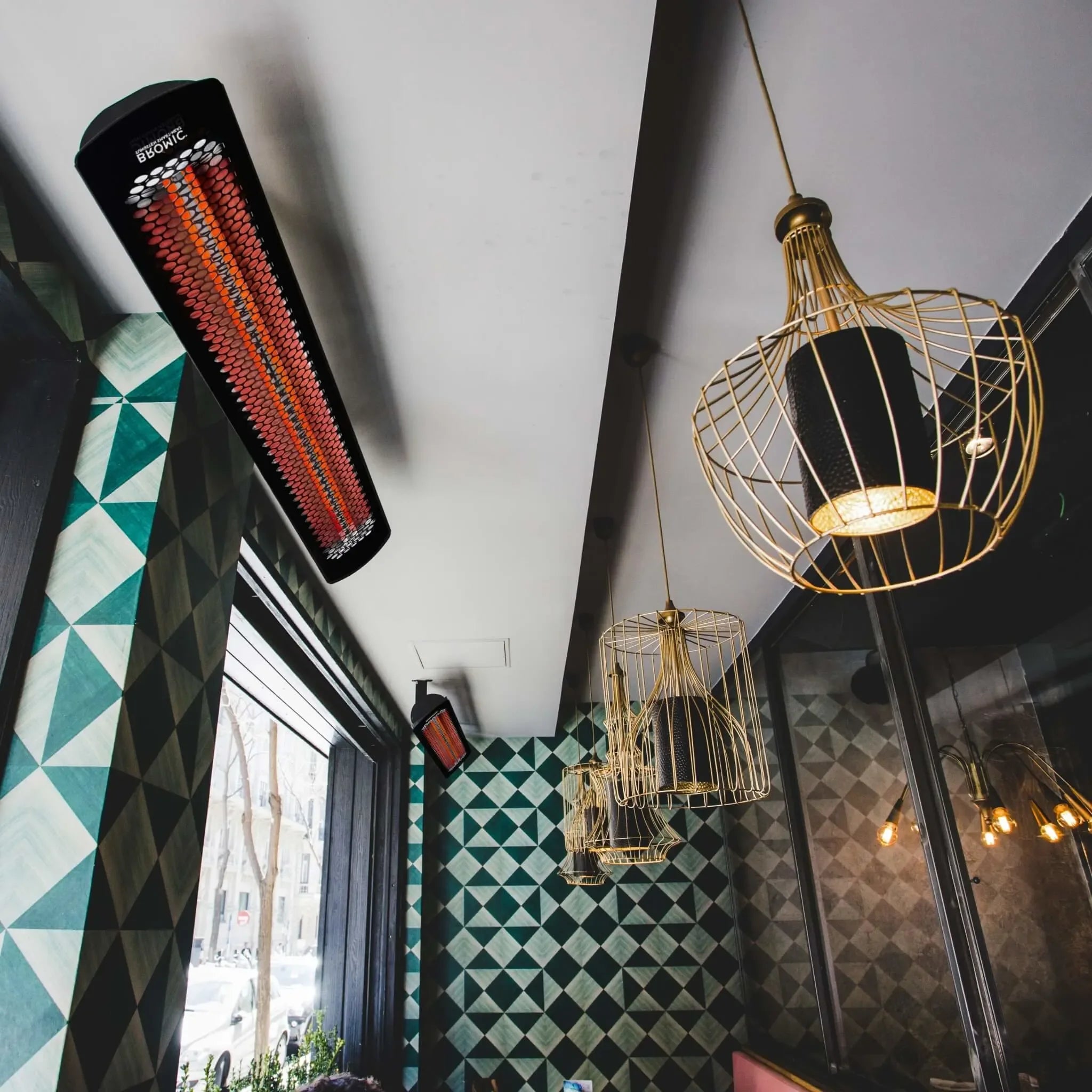Contemporary restaurant interior with ceiling-mounted Bromic Heating Tungsten Smart-Heat Electric Heaters, blending radiant warmth with modern décor and geometric wall patterns.