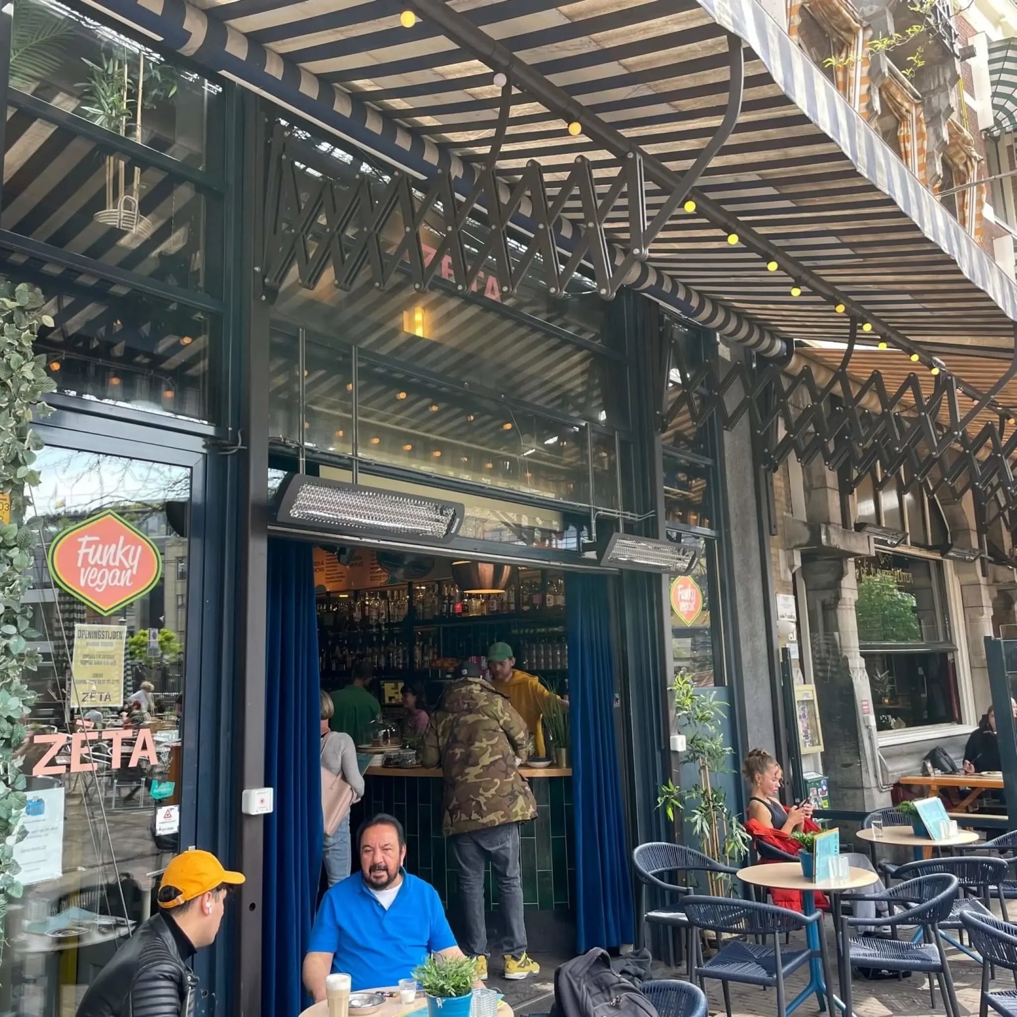 Restaurant patio entrance with Bromic Tungsten Electric Smart-Heat heaters wall-mounted above a striped canopy, keeping café guests comfortable while dining outdoors.