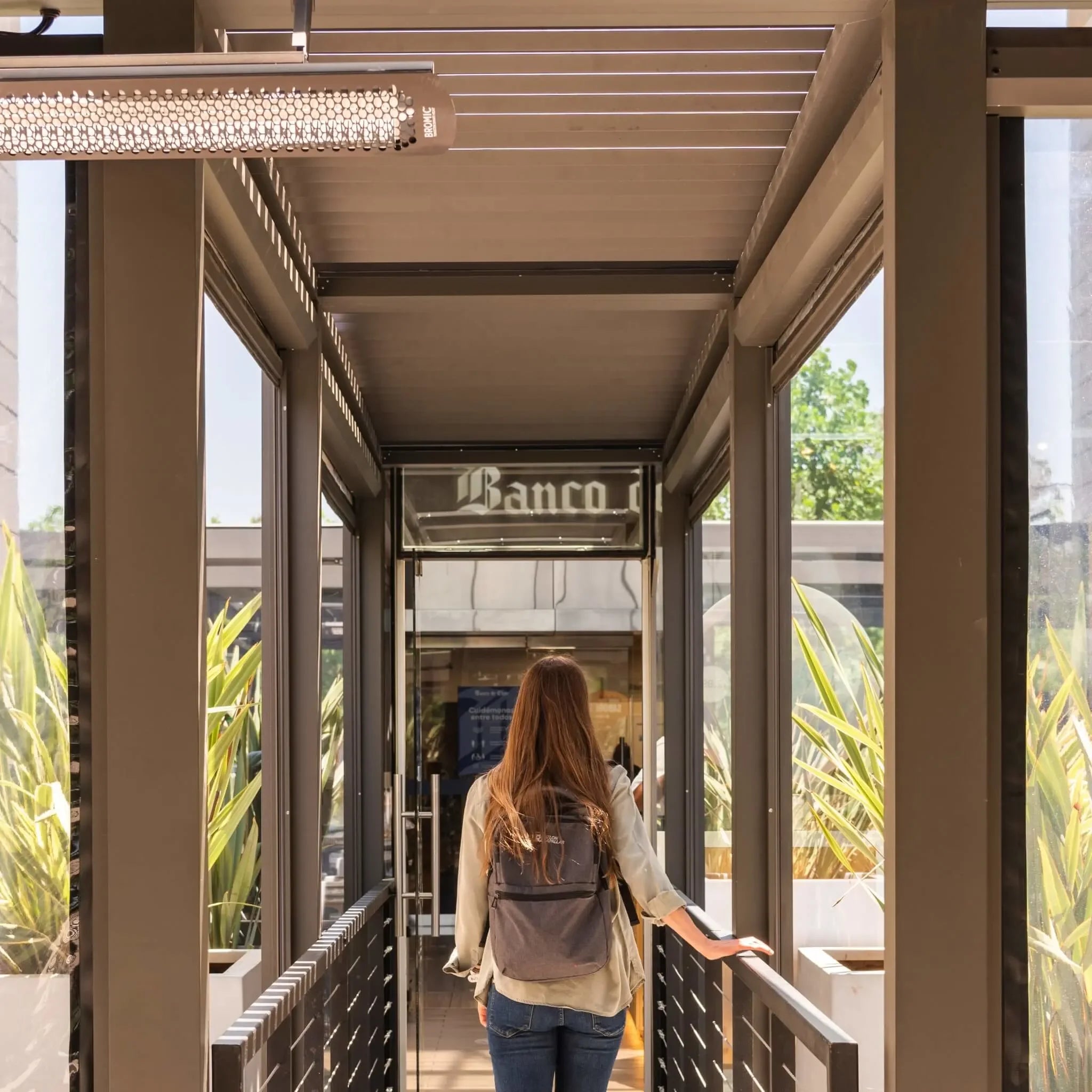 Outdoor walkway lined with Bromic Tungsten Electric Smart-Heat heaters mounted to a modern pergola, offering gentle radiant warmth for guests entering a restaurant.