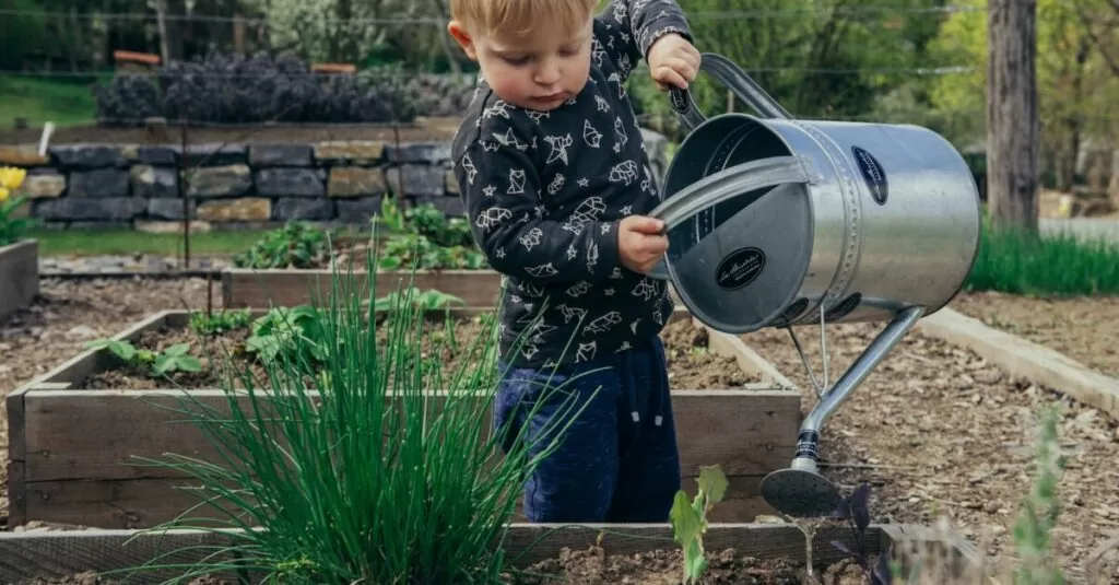 boy in black and white long sleeve shirt standing beside gray metal watering can during daytime