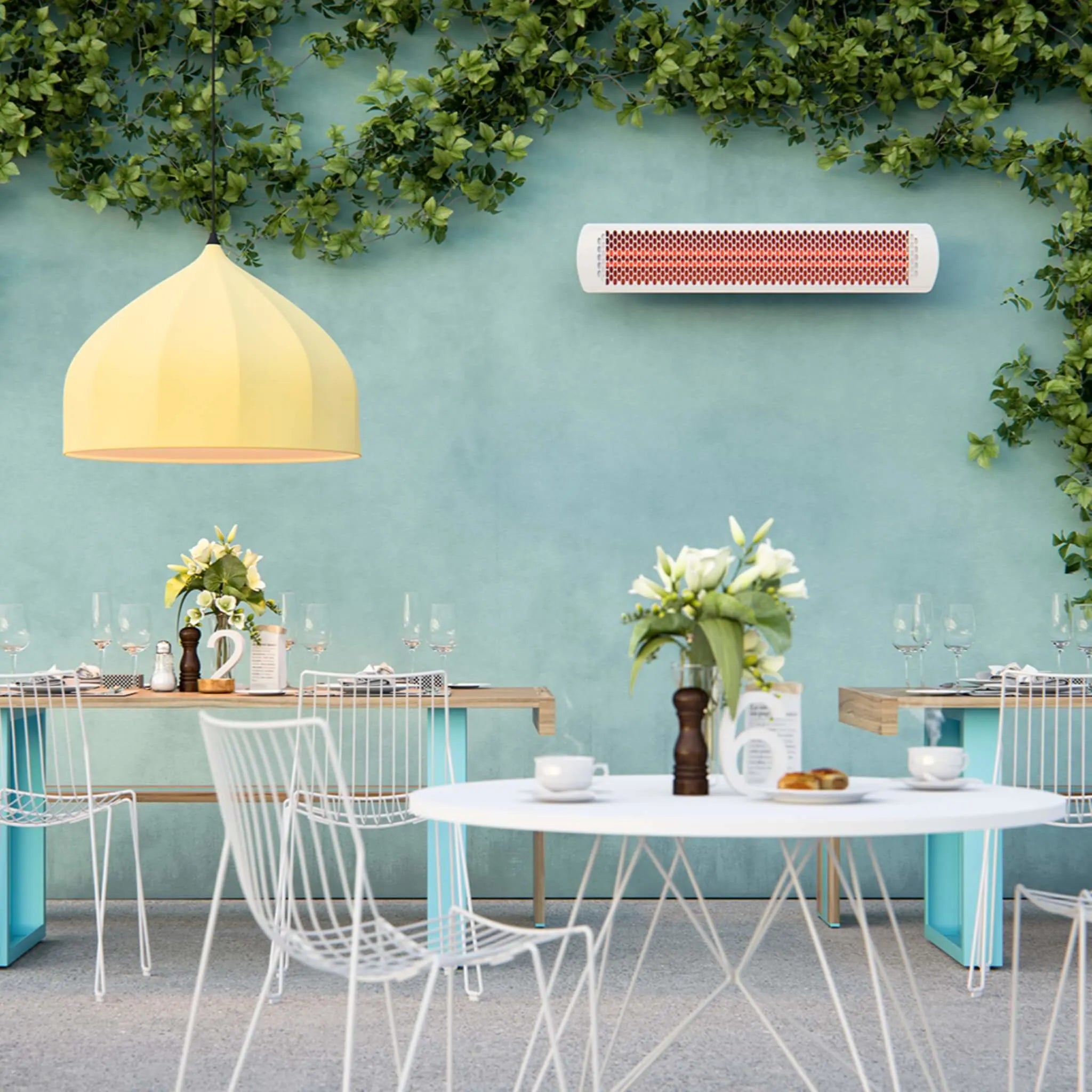 Outdoor bistro featuring Bromic Tungsten Electric Smart-Heat white wall-mounted heater on a mint-colored wall, adding warmth and style to a bright and airy dining space adorned with greenery.