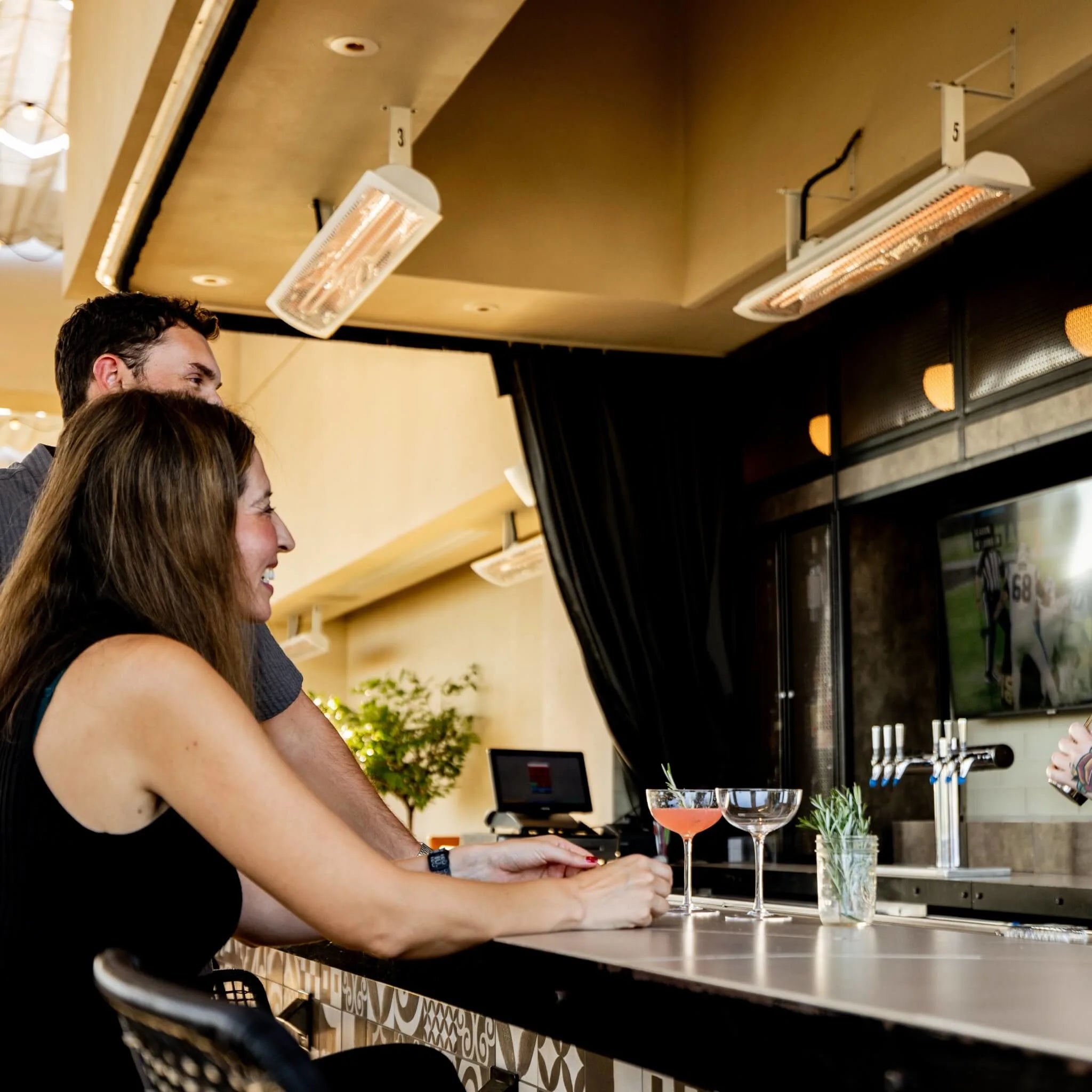 Contemporary commercial bar interior with Bromic Tungsten Electric Smart-Heat white heaters mounted above, providing efficient radiant warmth over a patterned tile bar and modern stools.